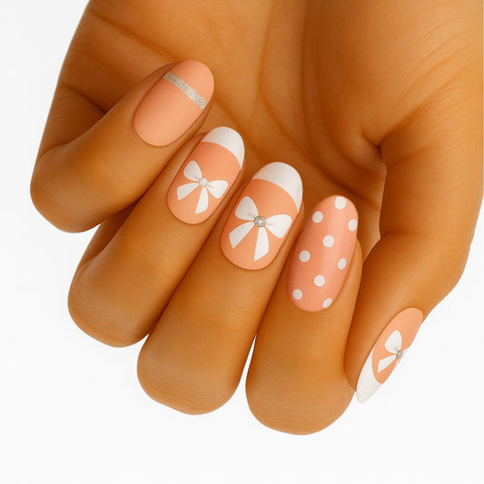Hand wearing peach nail wraps with white bow and polka dot patterns on short nails
