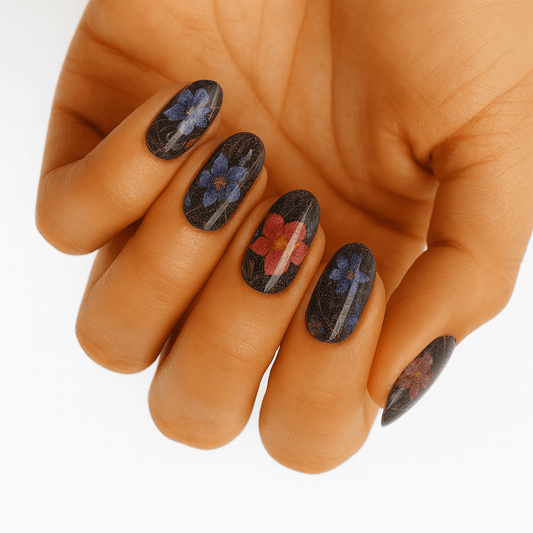 Hand wearing dark floral nail wraps with purple and red flowers on black background