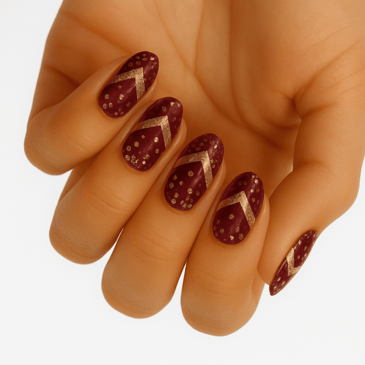 Hand displaying burgundy gel nail wraps with gold chevron patterns and glitter accents for festive manicure