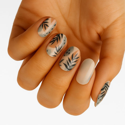 Matte beige nail wraps with black botanical leaf patterns on hand showing natural manicure design
