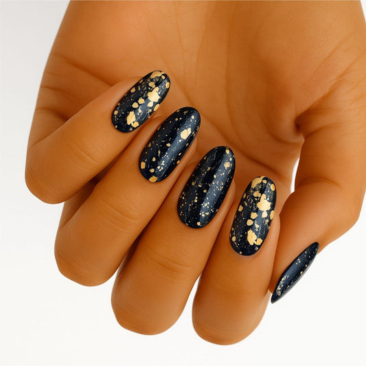 Hand wearing navy blue nail wraps with gold glitter speckles creating celestial night sky effect