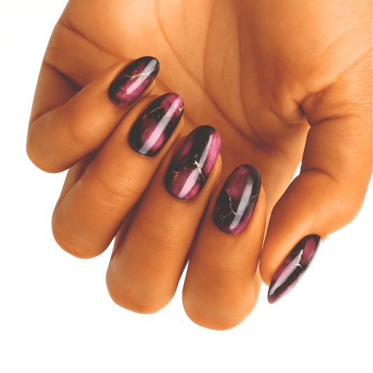 Hand displaying burgundy chrome nail wraps with marble veining and metallic finish