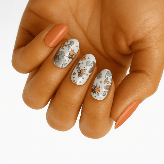 White nail wraps with peach floral bee pattern on hand showcasing botanical manicure design