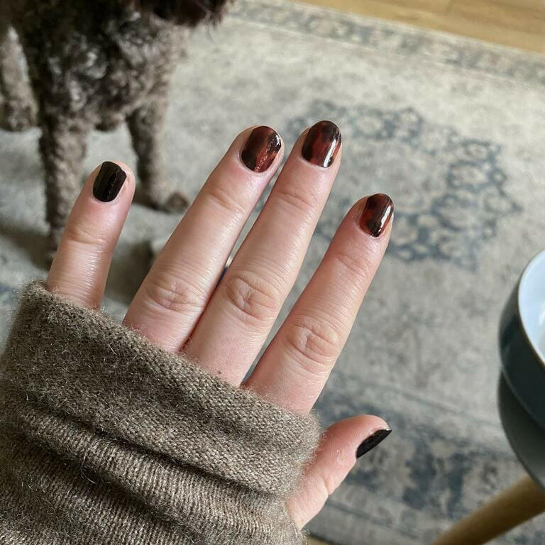 Hand wearing brown tortoiseshell nail wraps with black accent nail art