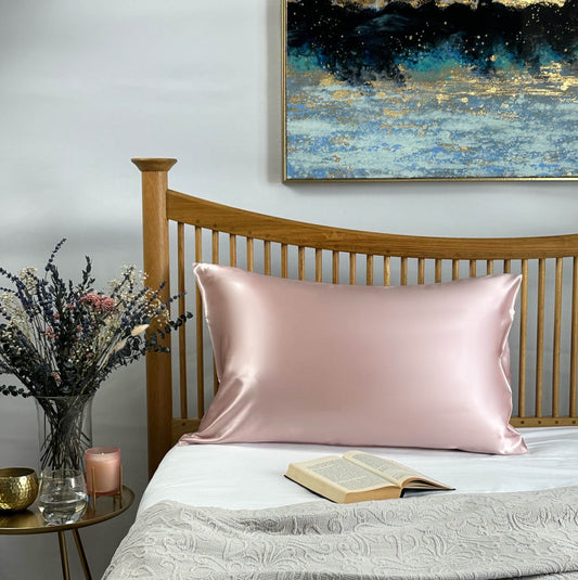 Pink silk pillowcase on wooden bed with flowers and book styling
