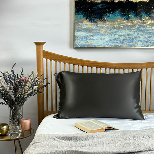 Forged grey silk pillowcase on wooden bed frame with book and vase styling