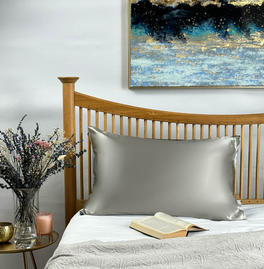 Light grey silk pillowcase styled on wooden bed with decorative accessories