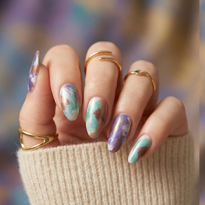 Multicoloured watercolour nail wraps in pastel purple blue and pink on hand with gold rings