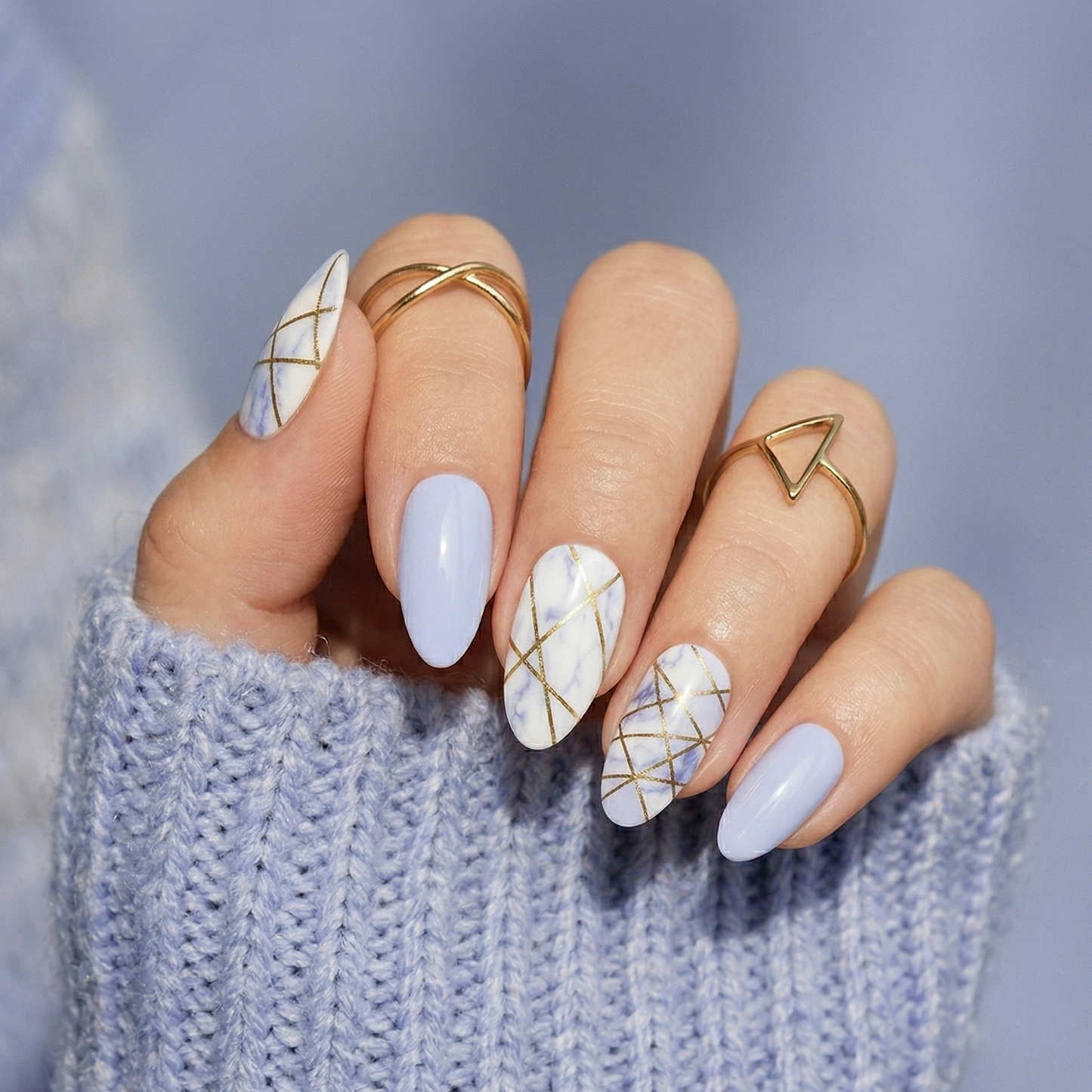 Blue marble geometric nail wraps with gold lines on hand in grey jumper