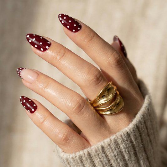 Burgundy press-on nails with white polka dots on hand wearing gold ring short almond shape