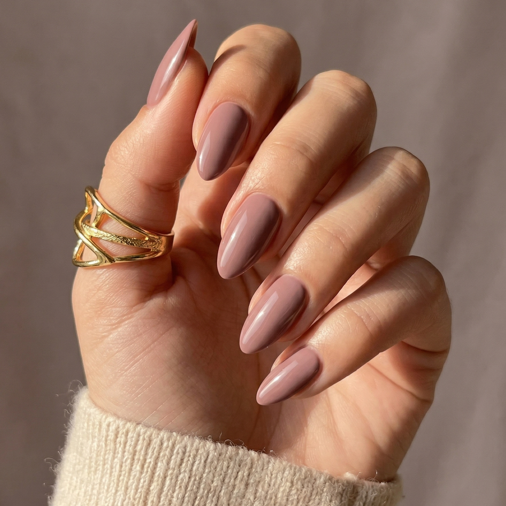 Dusty pink soft gel press-on nails in short almond shape on hand with gold ring