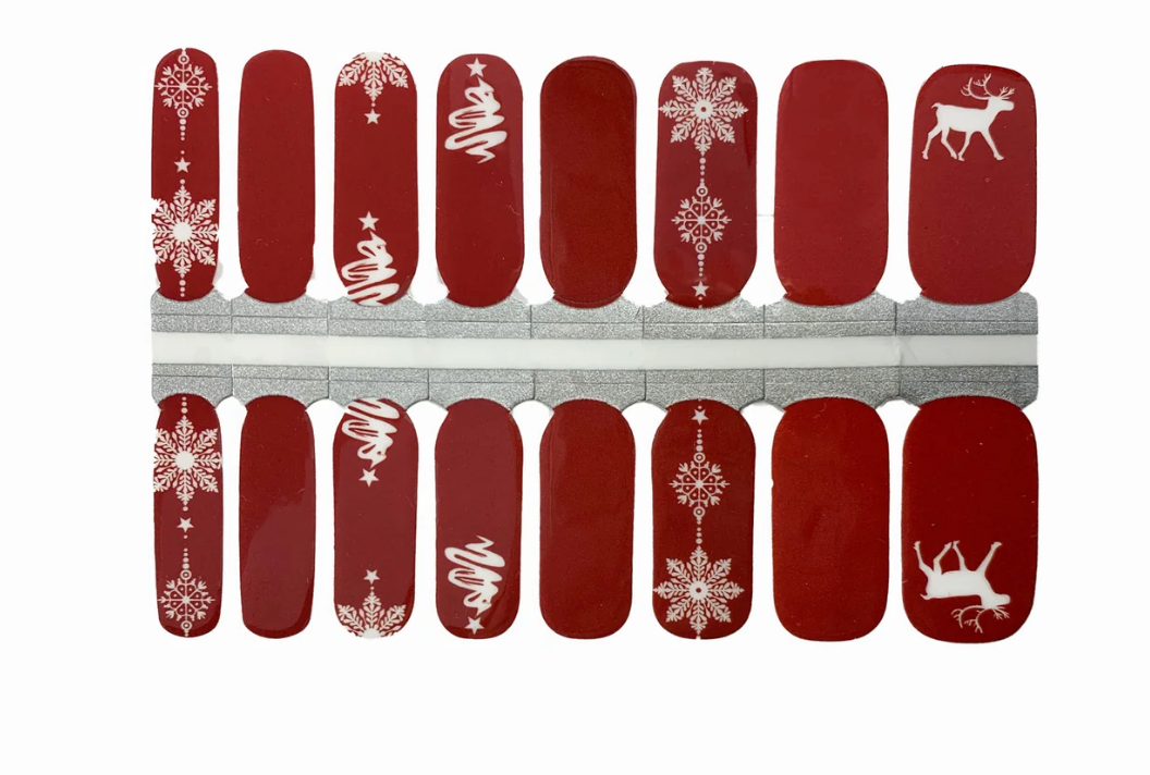 Red glossy nail wraps with white snowflakes, swirled trees, and reindeer Christmas design