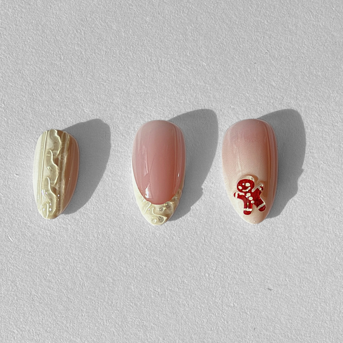 Nude pink soft gel press-on nails with cream icing swirl edging and gingerbread man design
