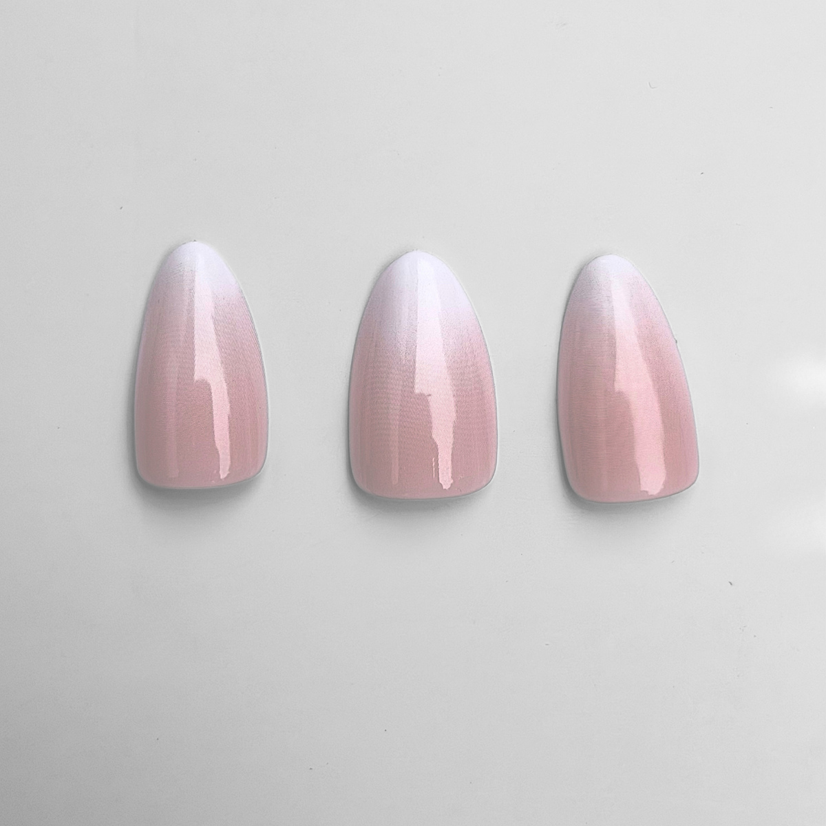 Glossy press-on nails, almond shape, pink-to-white ombre gradient design.