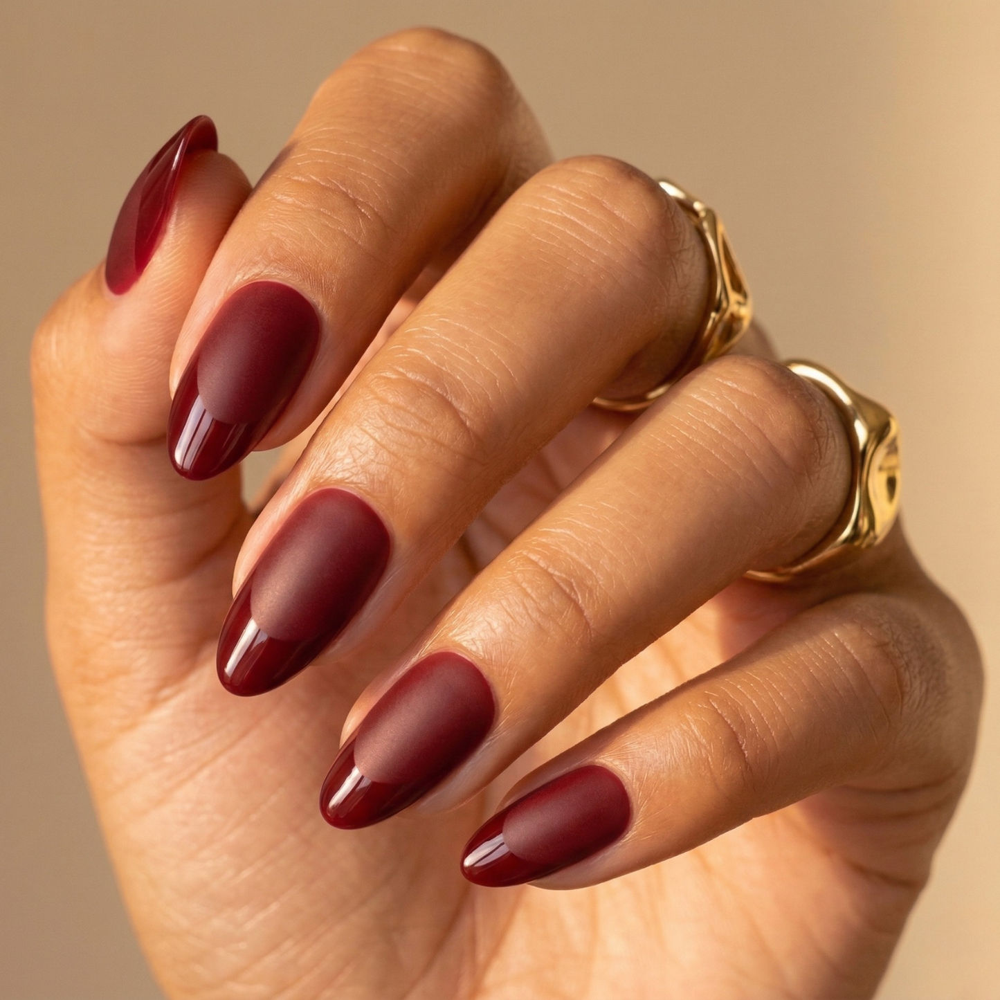 Deep burgundy red glossy press-on nails in short almond shape on hand with gold rings
