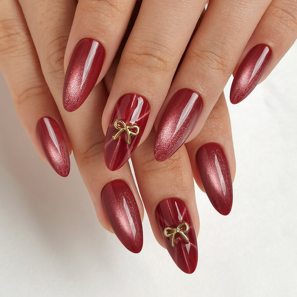Deep red cat-eye press-on nails, almond shape, with 3D gold bow charm accents