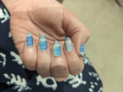 Hand wearing blue cloud nail wraps with pastel ombre gradient at-home manicure design