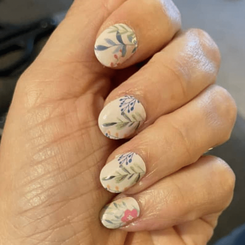 Cream botanical nail wraps with sage green floral patterns on hand manicure