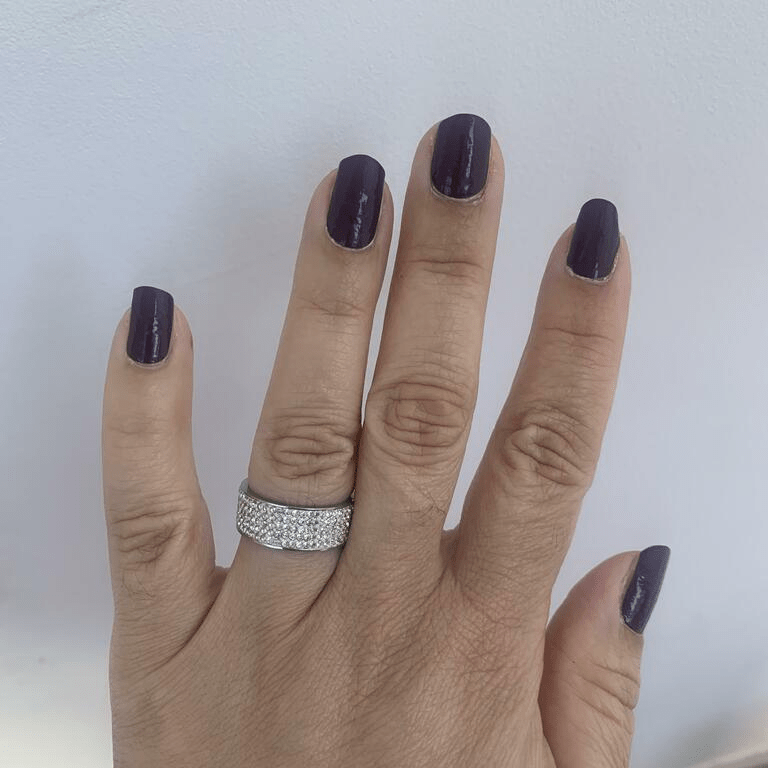 Dark purple glossy nail wraps on hand with diamond ring showing professional manicure