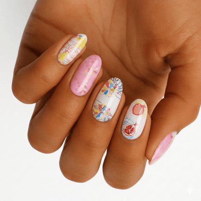 Hand wearing pastel nail wraps featuring fruit and floral designs in pink and peach tones