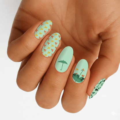 Spring nail art on hand featuring mint green nail wraps with orange birds and umbrella designs