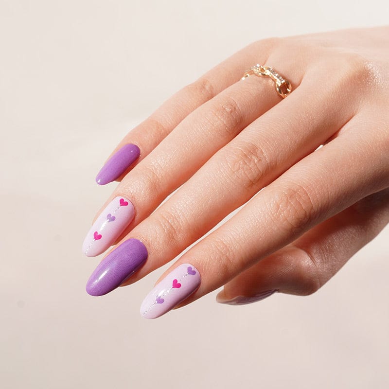 Hand wearing purple and pink heart pattern nail wraps with glossy finish