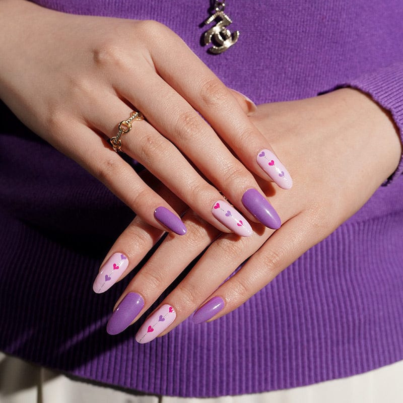 Purple jumper styled hands showing pink heart pattern nail wraps for Valentine's Day manicure