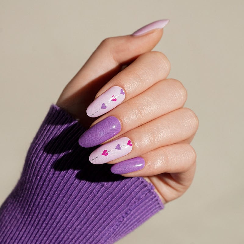 Hand wearing purple and pink heart nail wraps showing glossy romantic nail art design