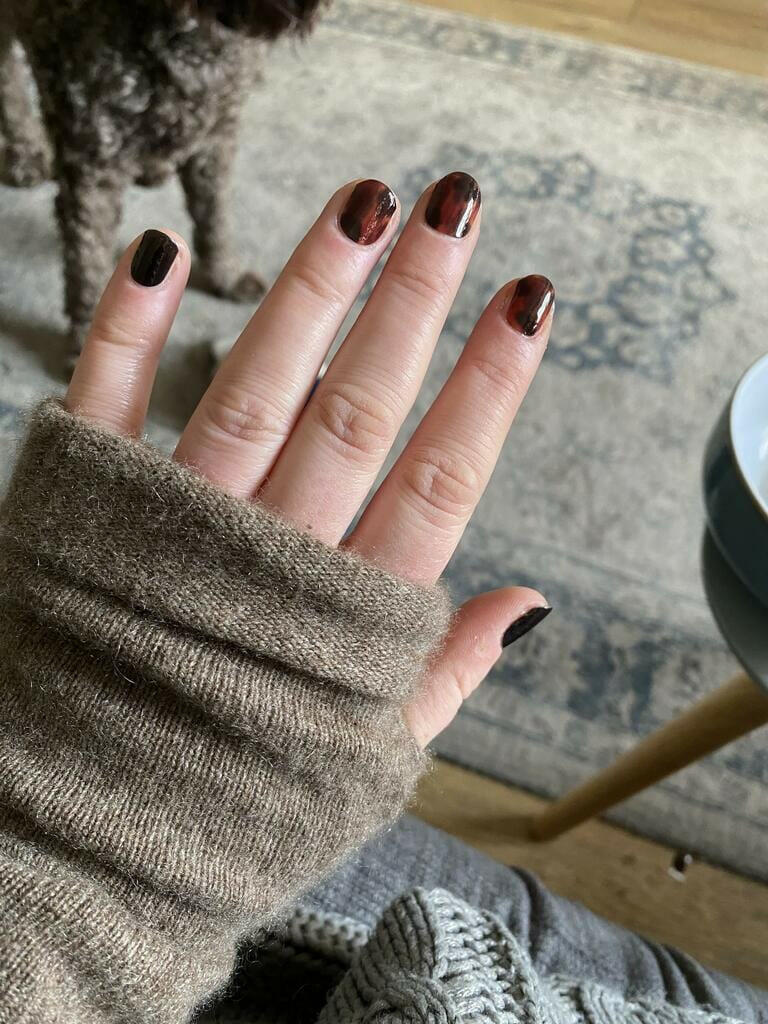 Hand wearing brown tortoiseshell nail wraps with black accent nail art