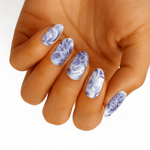 Hand displaying blue and white floral nail wraps with delicate porcelain swirl patterns