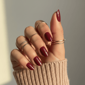 Hand wearing deep red glossy press-on nails in short oval shape with gold rings