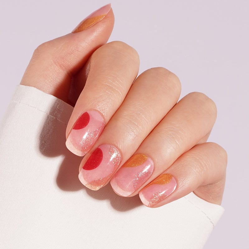 Hand with glossy gel nail wraps featuring abstract coral pink gold nail designs