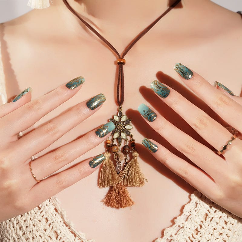 Sage green gel nail wraps with gold mandala pattern worn with bohemian tassel necklace